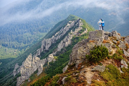 Travelers couple standing on rocky mountain summit, hugging and enjoying the view on beautiful valley.の写真素材