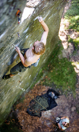 Young man lead climbing on large boulders marking the route, male partner belaying. Outdoor summer dayの写真素材