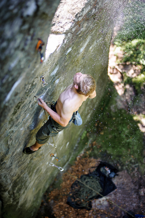 Young man rock-climbing on large boulder, blowing magnesium from fastening . Outdoor summer dayの写真素材