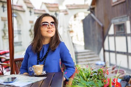 Young woman - teenage girl outdoors sitting at the cafe table with a cup of coffee and looking upの写真素材