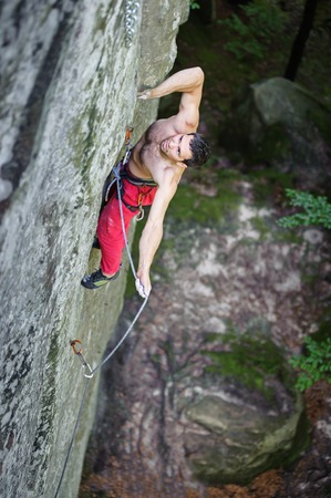 Young athletic man rock-climbing on large boulders with rope engaged. Outdoor summer dayの写真素材