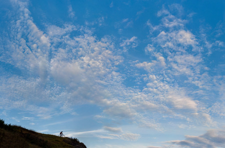 Silhouette of a cross country biker on the top of a hill against cloudy blue sky.の写真素材