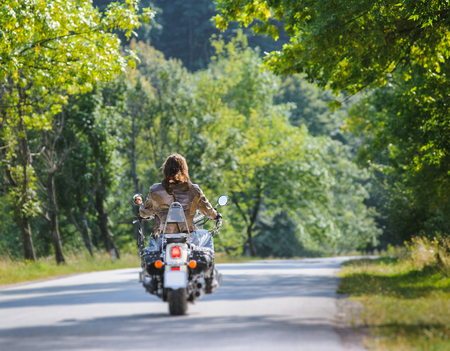 Biker with long hair riding motorcycle on road. View from the back. Tilt shift lens blur effectの写真素材