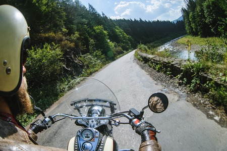 Biker in helmet driving his motorcycle on the open road by the river. First-person point of view. Focus is on the dashboard and handsの写真素材