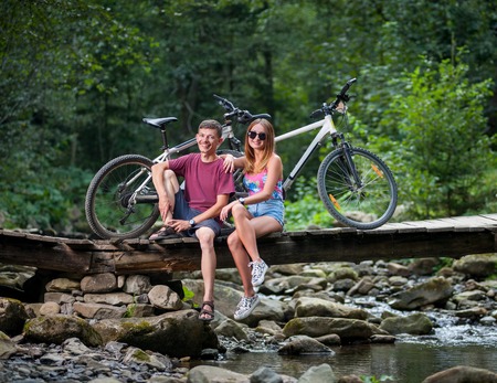 Young smiling happy couple resting in the forest on the river bridge near bicyclesの写真素材