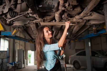 Portrait of sexy beautiful girl examining lifted car at the auto repair shopの写真素材