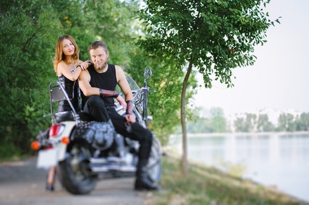 Portrait of attractive couple bikers standing by a cruiser motorbike near the lake on summer day. Tilt shift lens blur effect.の写真素材