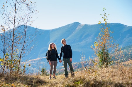 Young happy couple tourists holding hands smiling and looking into distance on a warm sunny autumn day in the mountains. Mountain on the background.の写真素材