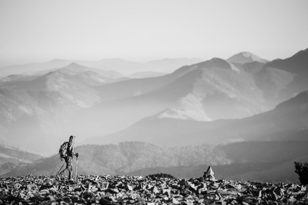 Hiker is walking on the rocky mountain on backpacking trip. Man is wearing jacket and backpack on. Beautiful mountains on background. Ecotourism and healthy lifestyle concept. black and whiteの写真素材