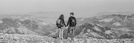 Rear view of young couple hikers with backpacks standing on the ridge of the mountain, enjoying the...
