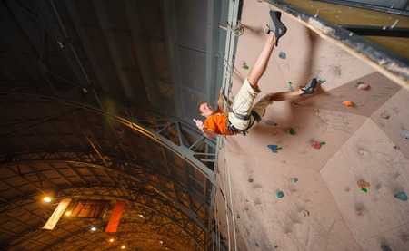 Young man climbing on practical wall in gym, bouldering. Giving thumb up and smiling.の写真素材