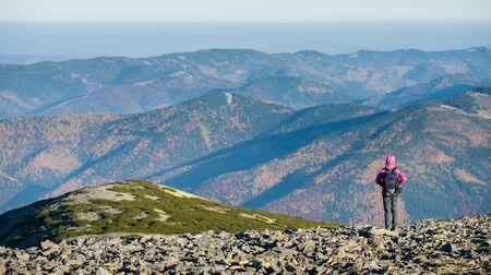Female hiker standing on mountain plato enjoying beautiful overlook on the mountains with backpack on. Rear view. Ecotourism and healthy lifestyle concept. Copy space.の写真素材