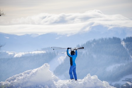 Rear view of skier standing on top of the mountain and enjoying the view on beautiful winter...