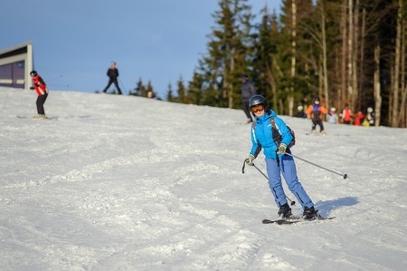 Female skier skiing downhill at ski resort. Woman is wearing blue ski suit helmet and goggles on sunny day. Ski holidays.の写真素材