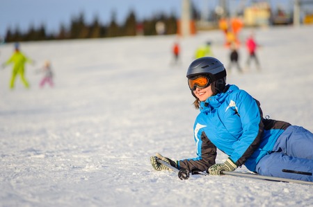 Young skier woman in blue ski suit orange goggles and helmet lying on the snow at ski resort on a sunny day. Ski vacation.の写真素材