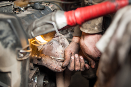 Close-up detail shot of car mechanic dirty hands. Worker repairing broken motor in garage using socket wrenchの写真素材