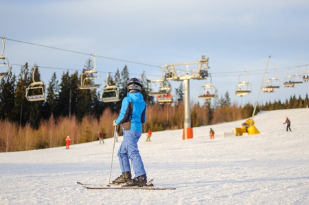 Side view of female skier standing on a ski slope with ski-lift, forest and beautiful sky on the background in the evening. Winter sports concept. Carpathian Mountains, Bukovel, Ukraineの写真素材