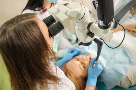 Female dentist checking patient teeth, looking in dental mirror through the microscope. Dental care...