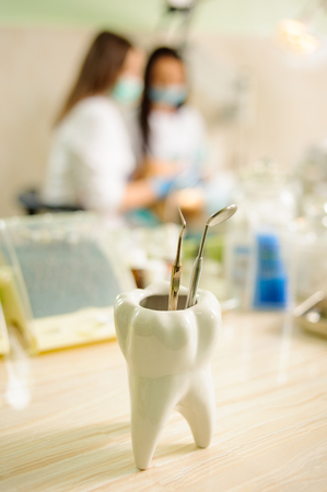 Dentistry tools on foreground and female dentist with assistant doing first check-up on the background. Specialized medical equipment in the dental officeの写真素材