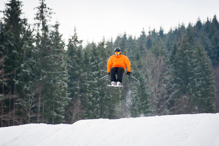 Flying skier at jump from the slope of mountains in orange jacket performing a high jump, with forest in background. Carpathian Mountains, Bukovelの写真素材