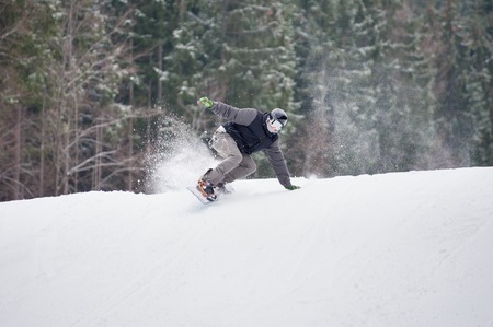 Male snowboarder rides over fresh snow powder on the slope in winter with snow-covered firs in background, extreme sportの写真素材