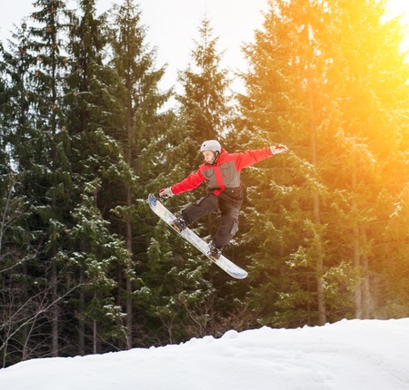 Male boarder  jumping and keeps one hand on the snowboard over the slope in winter with snowy slope and snow-covered firs in background, extreme sportの写真素材