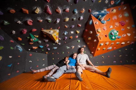 Two tired guys and one girl with closed eyes sitting on the orange mat near rock wall indoors. Boulderingの写真素材