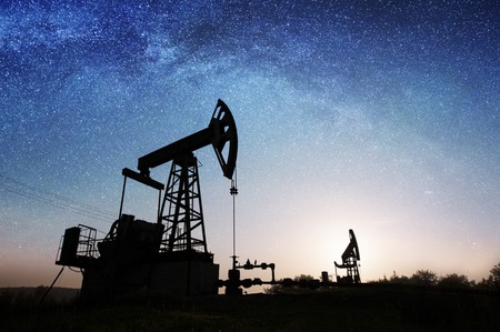 Silhouette of two oil pumps are pumping crude oil on the oil field under night sky with stars and Milky way. Oil industry equipmentの写真素材