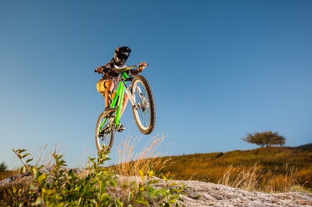 Cyclist in helmet and glasses jumping on a mountain bike on the hill against blue sky. Dangerous downhill. Bottom viewの写真素材