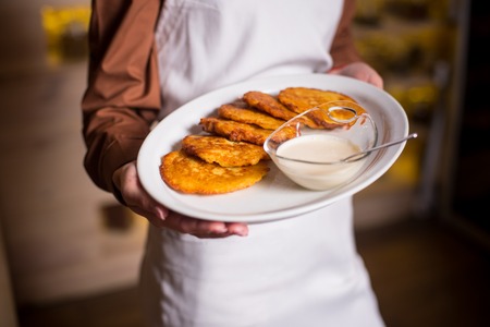Potato pancakes served on white plate with sour creamon a white plate in hand of woman with white apron. Close-upの写真素材