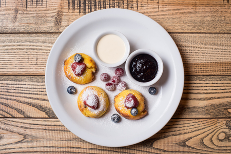 Cottage cheese pancakes served with berries blueberries, raspberries, sauce and jam on a white plate at the rustic wooden background. Selective focus top viewの写真素材