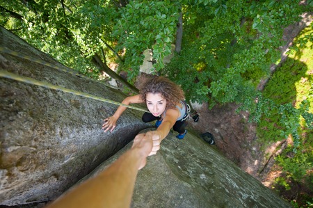 A athletic rockclimber is helping a beautiful woman climber to reach a top of the high wall. Man...