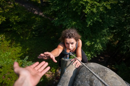 Young fearless woman climbing on large boulder, her male partner giving her a hand. Helping hand. View from the topの写真素材