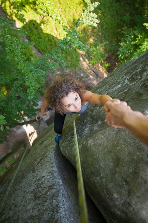 Top view of brave climber girl climbing on big rock and hanging on the hand. Man giving a hand to the woman. View from the topの写真素材