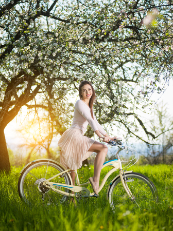 Beautiful woman wearing white dress sitting astride on bicycle and sexually posingの写真素材