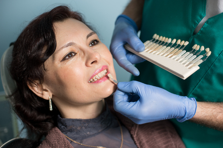 Close-up portrait of woman in dental clinic office. Dentist checking and selecting colour of the teeth, making the process of treatment. Dentistryの写真素材