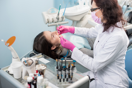 Female dentist with dental tools - mirror and probe treating patient teeth at dental clinic office. Medicine, dentistry and health care concept. Dental equipmentの写真素材
