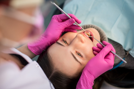 Close up of beautiful young woman having dental check up in dental office. Dentist examining a patient's teeth with dental tools - mirror and probe. Dentistry.の写真素材