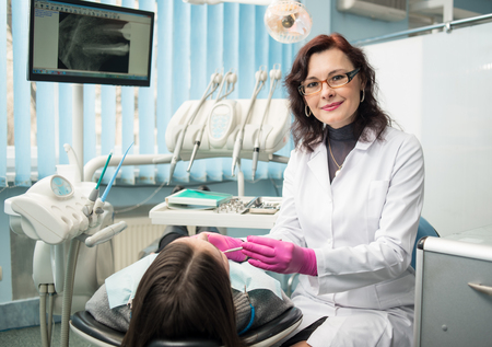 Female dentist with dental tools - mirror and probe treating patient teeth and looking to the camera at dental clinic office. Medicine, dentistry and health care concept. Dental equipmentの写真素材