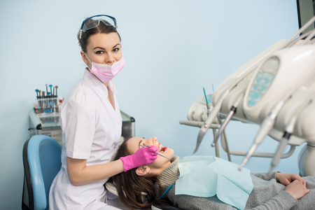 Female dentist with dental tools - mirror and probe checking up patient teeth and looking to the camera at dental clinic office. Medicine, dentistry and health care concept. Dental equipmentの写真素材