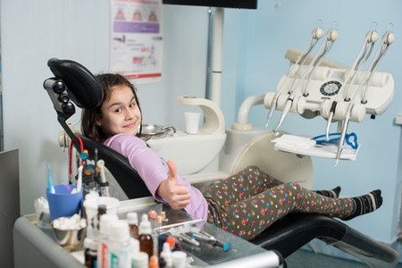 Happy patient girl showing thumbs up at dental clinic office. Medicine, stomatology and health care concept. Dental equipmentの写真素材