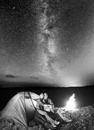 Young pair hikers looking to the shines starry sky and Milky way in the camping at night near campfire. Long exposure. Black and whiteの写真素材