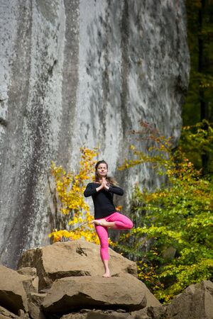 Sporty slim woman is practicing yoga and doing asana Vrikshasana on the boulder in the nature. Huge rocks on the backgroundの写真素材