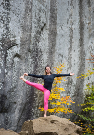 Active fit woman is practicing yoga on the boulder in the nature. Huge rocks on the backgroundの写真素材