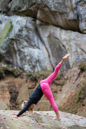 Attractive fit woman is practicing yoga and doing asana Adho Mukha Shvanasana in the nature. Huge rocks on the backgroundの写真素材