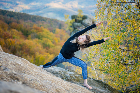 Flexible young woman is practicing yoga on the top of the high rocky mountain. Autumn forests, rocks and hills on the backgroundの写真素材