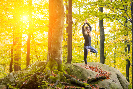 Yoga outdoors - sporty fit woman doing asana Vrikshasana in the autumn forest on the top of big boulderの写真素材
