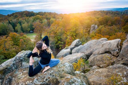 Flexible young woman is practicing yoga and doing asana Eka Pada Rajakapotanasana on the top of the...