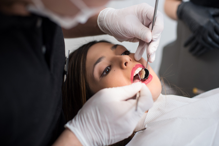 Close up of beautiful young woman having dental check up in dental clinic. Dentist examining a patient's teeth with dental tools - mirror and probe. Dentistry.