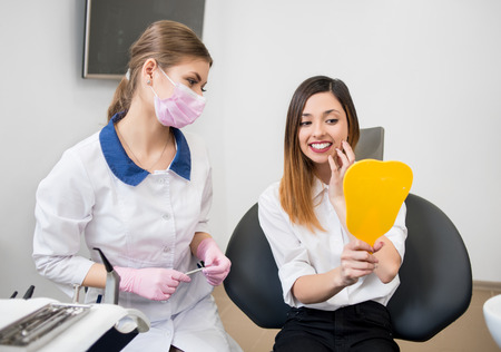 Young happy woman with female dentist checking their teeth at mirror after dental procedure in dental clinic. Dentistryの写真素材